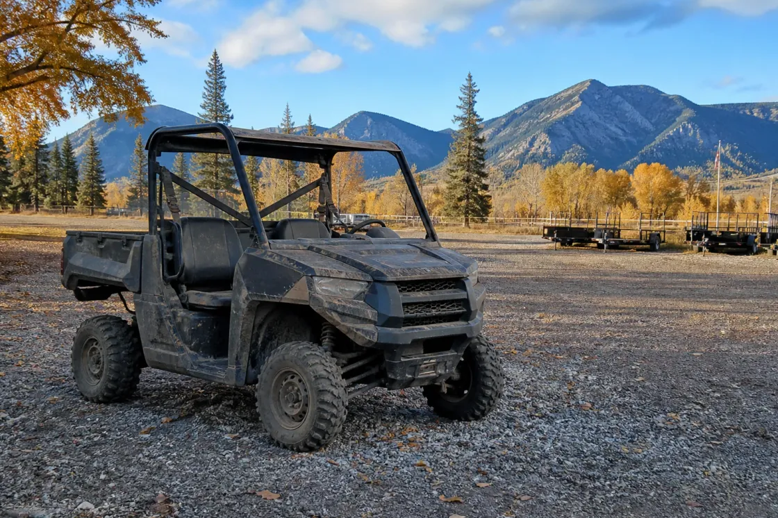 A utility side-by-side vehicle parked on a gravel lot in rural Alberta with foothills in the background