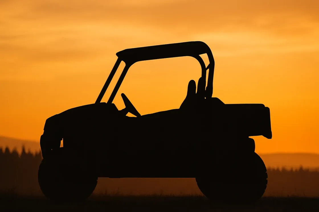 A side-by-side UTV in silhouette against a golden-hour sky in the Alberta foothills, with prairie grass in the foreground and a spruce treeline on the horizon