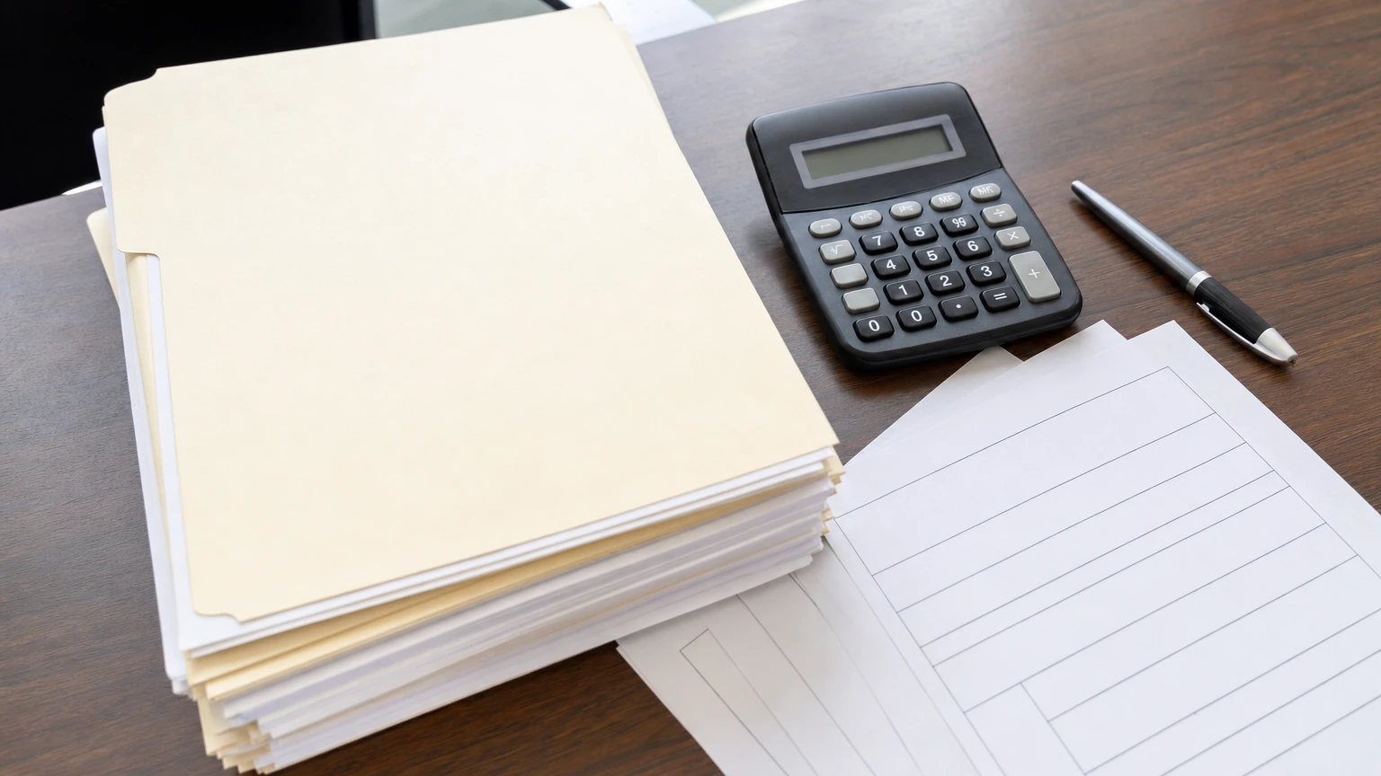 A wood dealership desk with a stacked loan folder, blank forms, calculator, and pen ready for review
