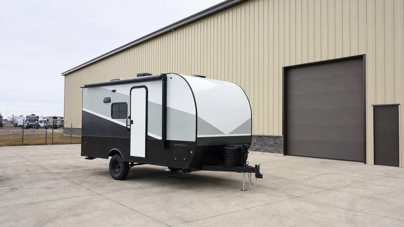 A clean towable camper trailer parked on a shop pad during a walk-around inspection in bright overcast daylight